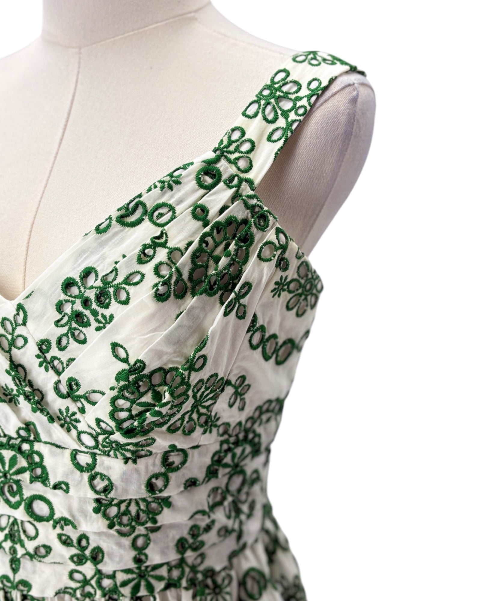 White dress with green floral embroidery on a mannequin against a white background