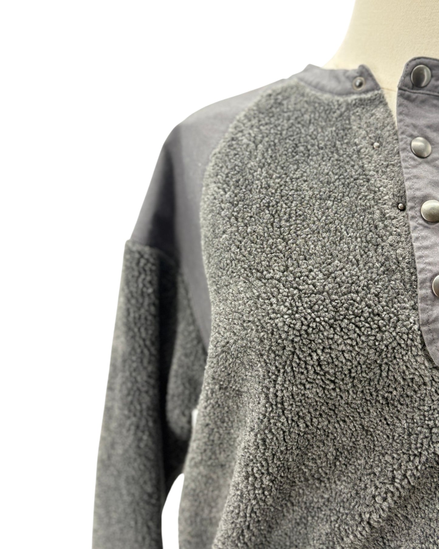 Close-up of a gray fleece pullover sweater with a buttoned collar and contrasting smooth gray shoulder panels, displayed on a mannequin against a white background.