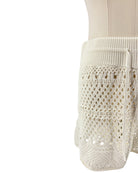 Close-up of a white knitted garment with lace detailing on a white background