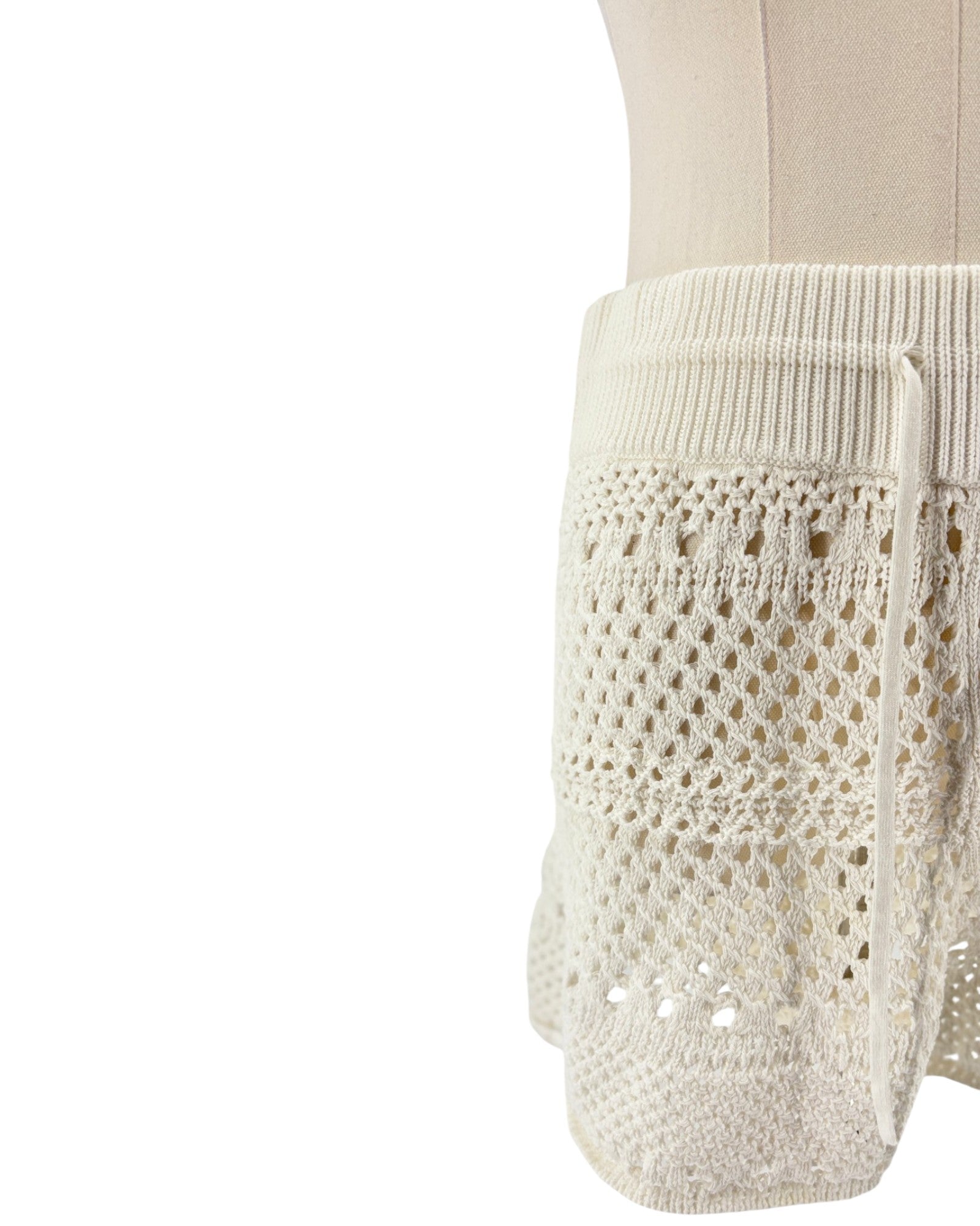Close-up of a white knitted garment with lace detailing on a white background