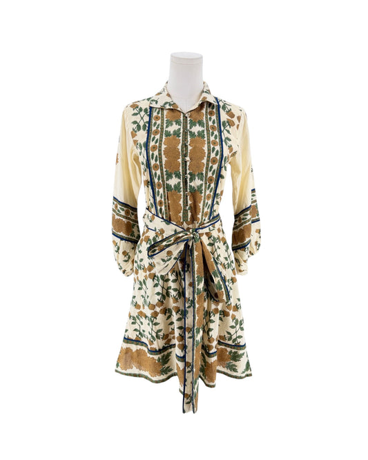 A long-sleeve collared shirt dress with a tie waist, displayed on a mannequin against a plain white background. The dress features a cream base with a brown and green botanical pattern.