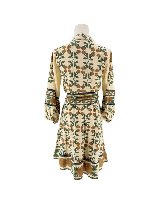 A cream-colored long-sleeve dress with a green and brown floral pattern, displayed on a mannequin from the back against a white background.