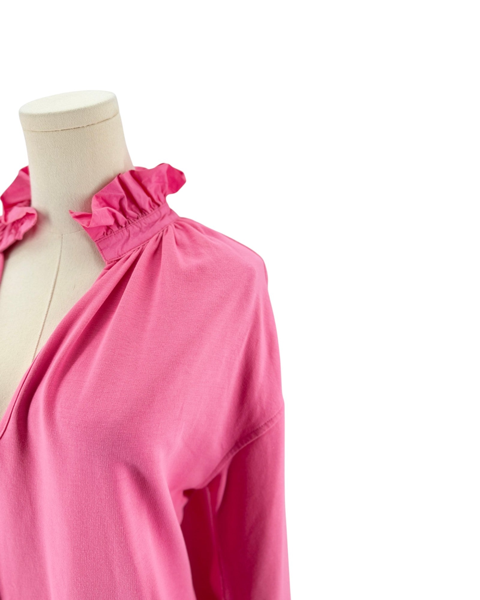 A bright pink long-sleeve dress with a ruffled smocked neckline, displayed on a cream dress form against a white background.