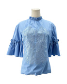 Blue blouse with intricate white embroidery on a mannequin against a white background
