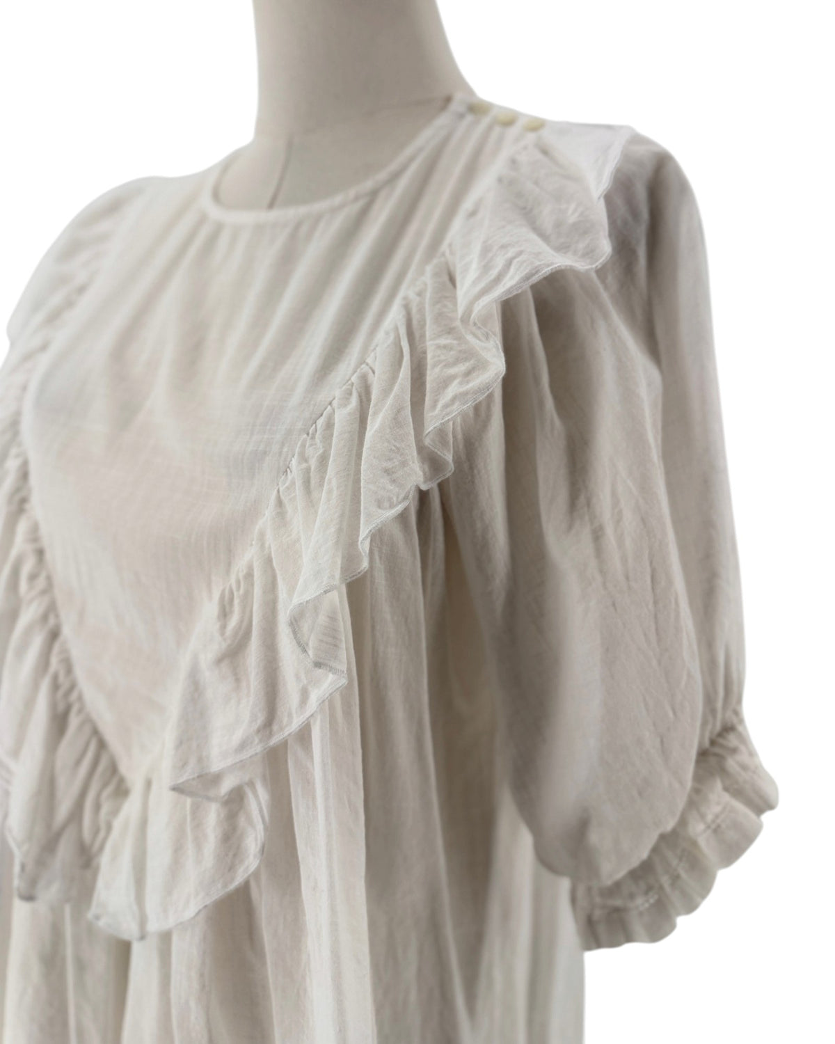 White ruffle triangle top, v-shaped ruffle down the body, voluminous short sleeves, round neckline on a mannequin on a white background