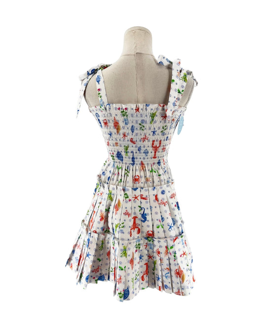 A sleeveless smocked dress with tie shoulder straps, featuring a colorful print of sea creatures like starfish, crabs, and fish on a white background, displayed on a mannequin torso against a white background.