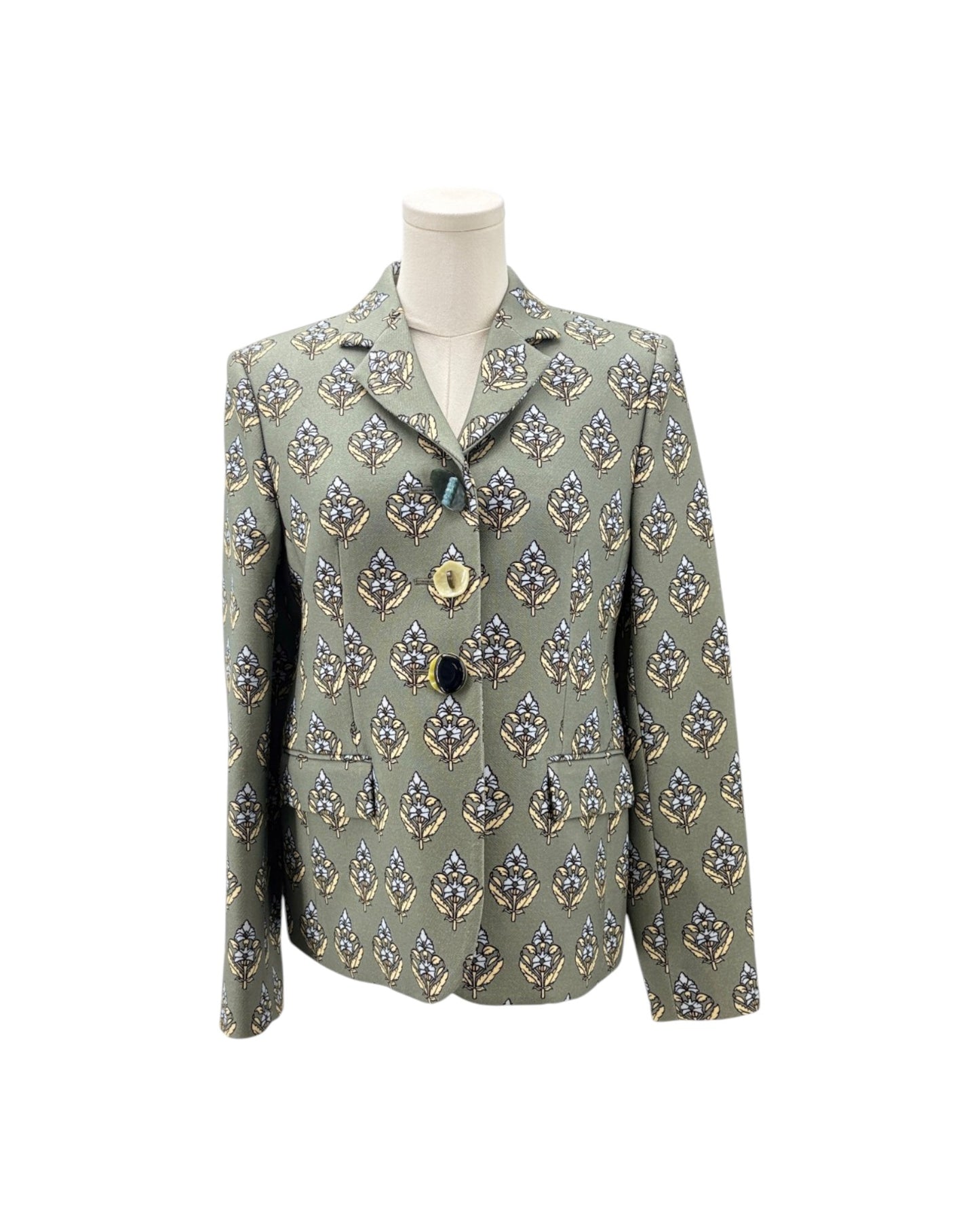 A women's tailored blazer jacket displayed on a mannequin torso against a plain white background. The jacket features a muted sage green base with an all-over repeating pattern of stylized floral or leaf motifs in navy blue, gold, and white.