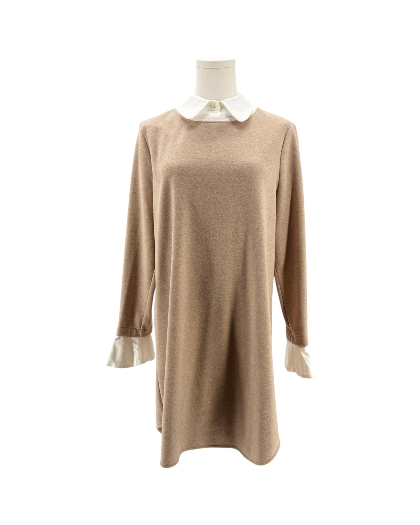 A beige knit long-sleeve tunic dress displayed on a mannequin, featuring a contrasting white collar and white ruffled cuffs.
