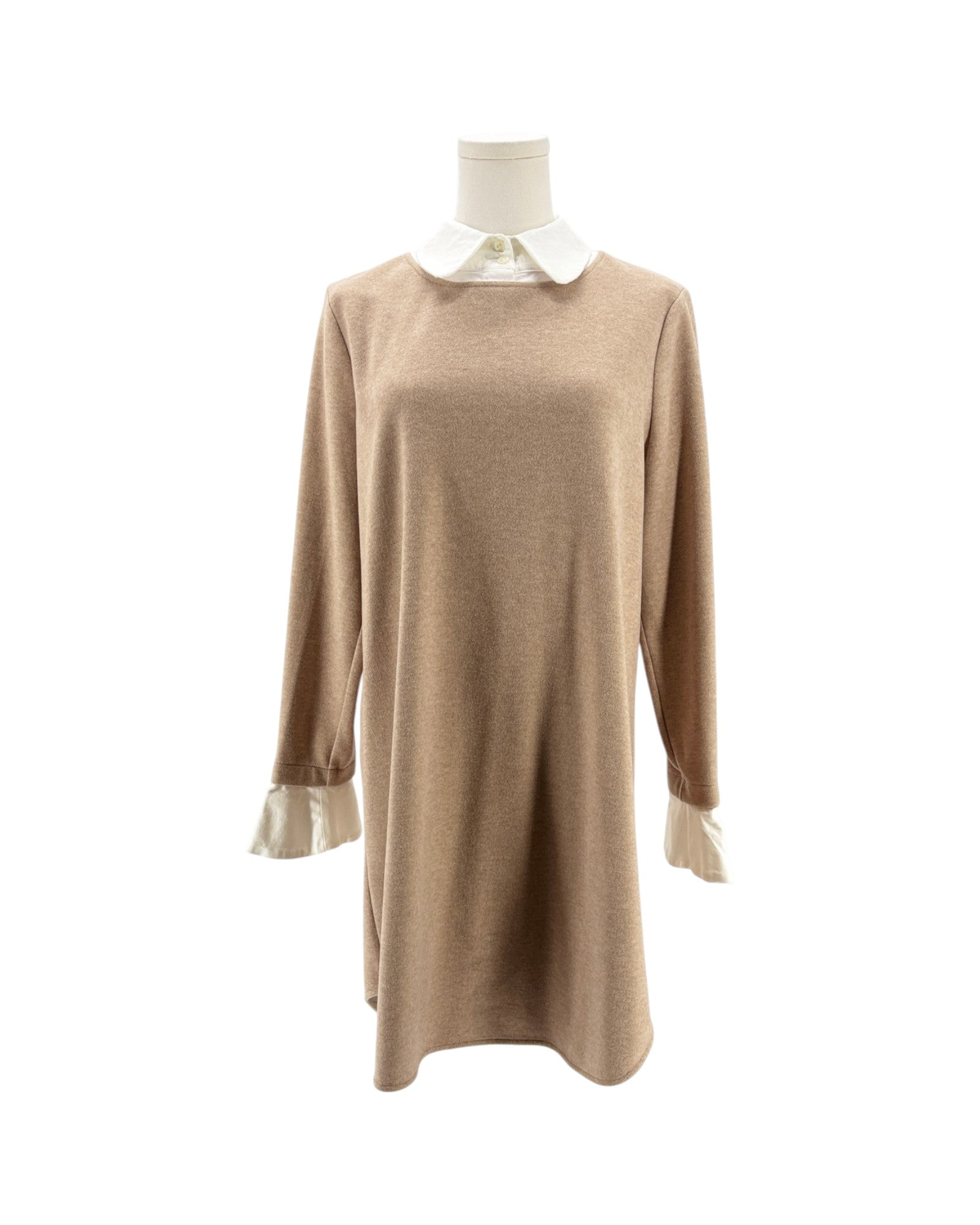 A beige knit long-sleeve tunic dress displayed on a mannequin, featuring a contrasting white collar and white ruffled cuffs.