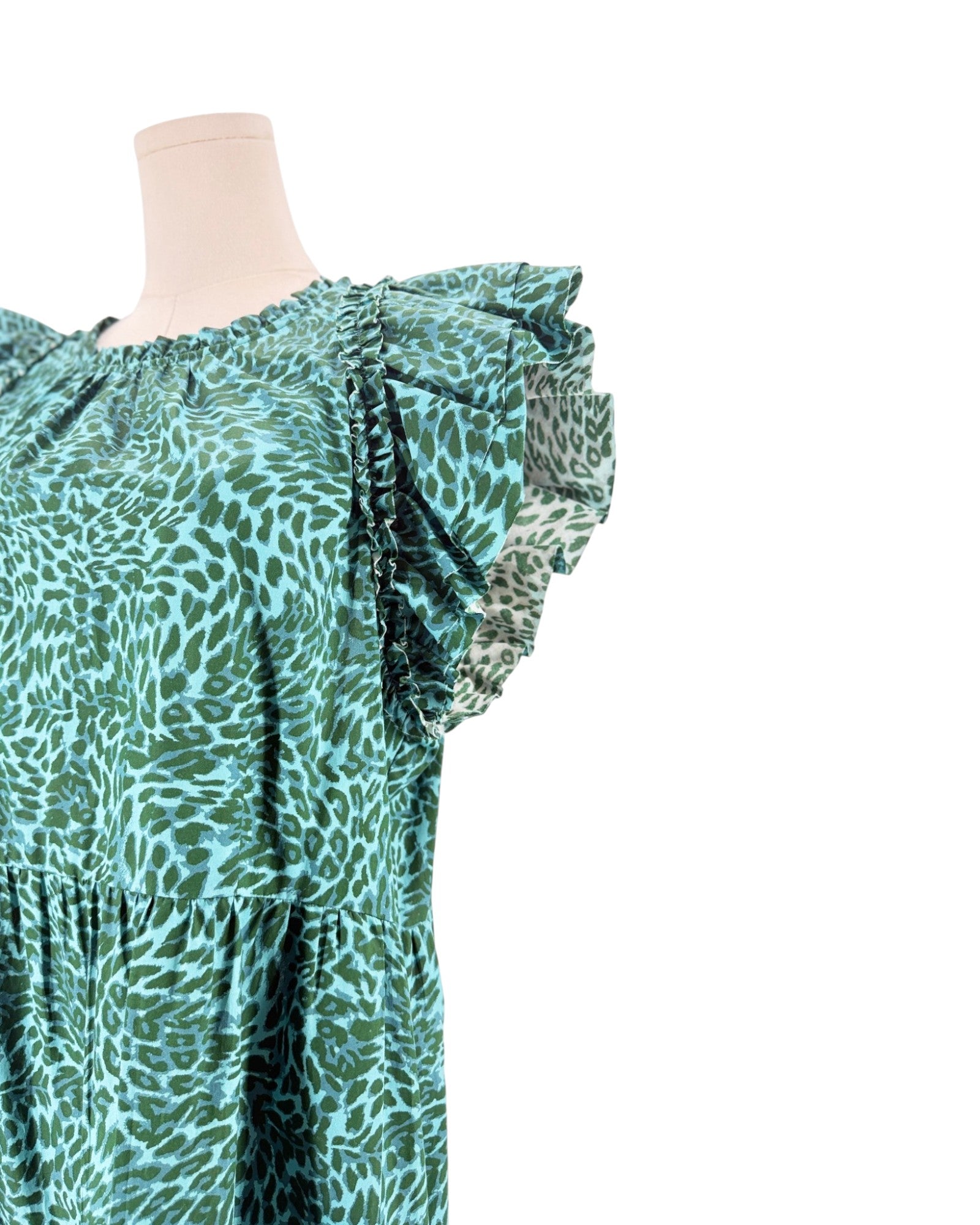 A close-up of a green and teal animal print dress on a mannequin torso, featuring ruffled cap sleeves and a tiered waist, set against a plain white background.