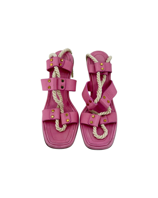 A pair of pink leather sandals featuring thick beige rope details woven through the straps and gold-tone metal studs, shown against a plain white background.
