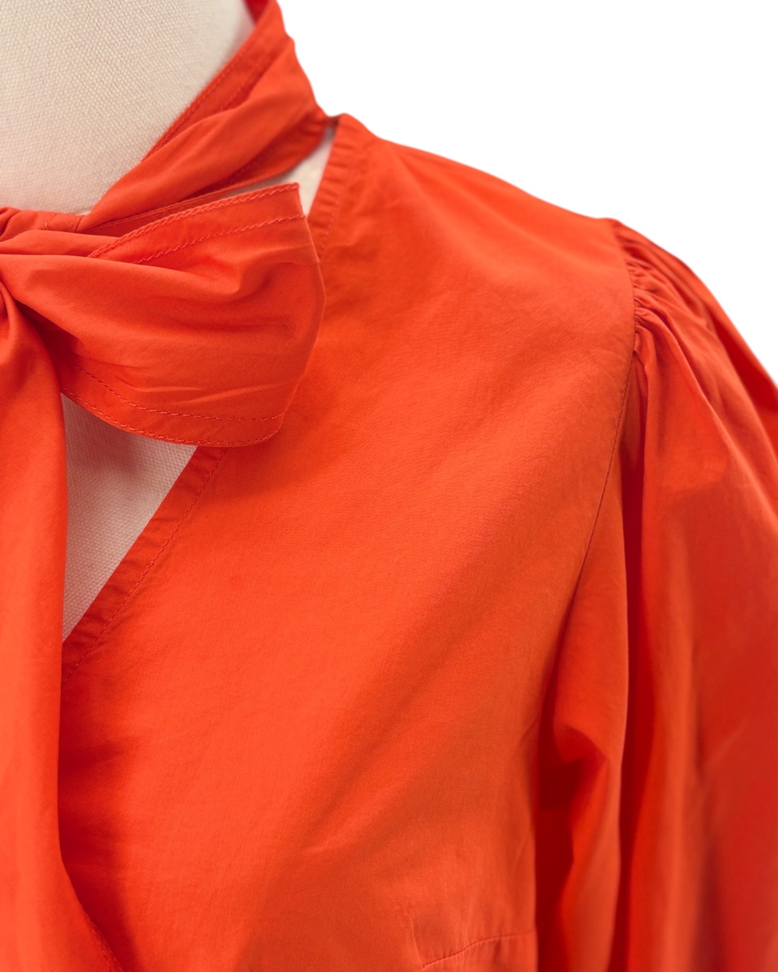 Orange blouse with a bow detail on a mannequin against a white background