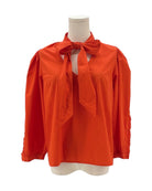 Orange blouse with a bow tie on a mannequin against a white background