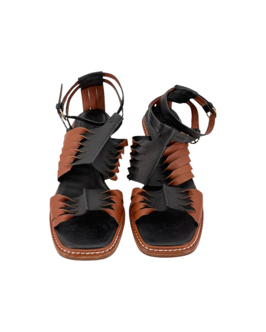 A pair of women's strappy sandals with a unique layered design featuring brown leather and black suede-like panels, set against a plain white background.