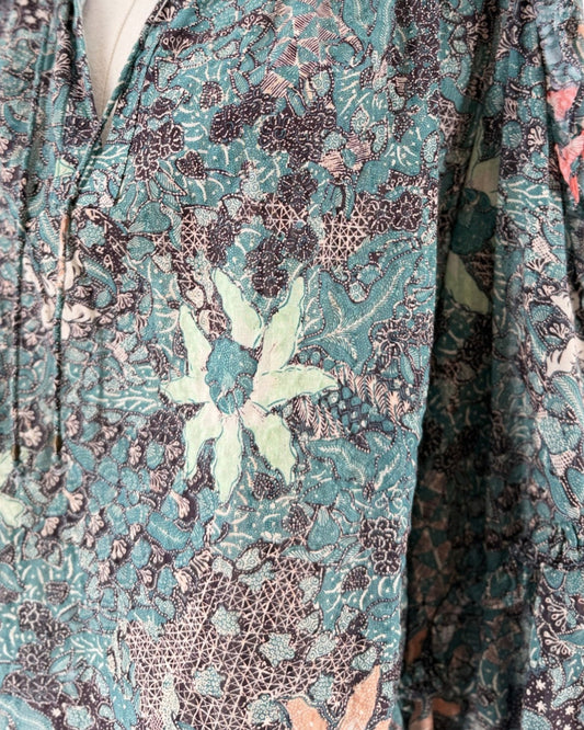 Multi color geometric floral print, full length sleeves with cascade sleeves finished with elastic cuff, v-neckline with tassel detail on a mannequin on a white background