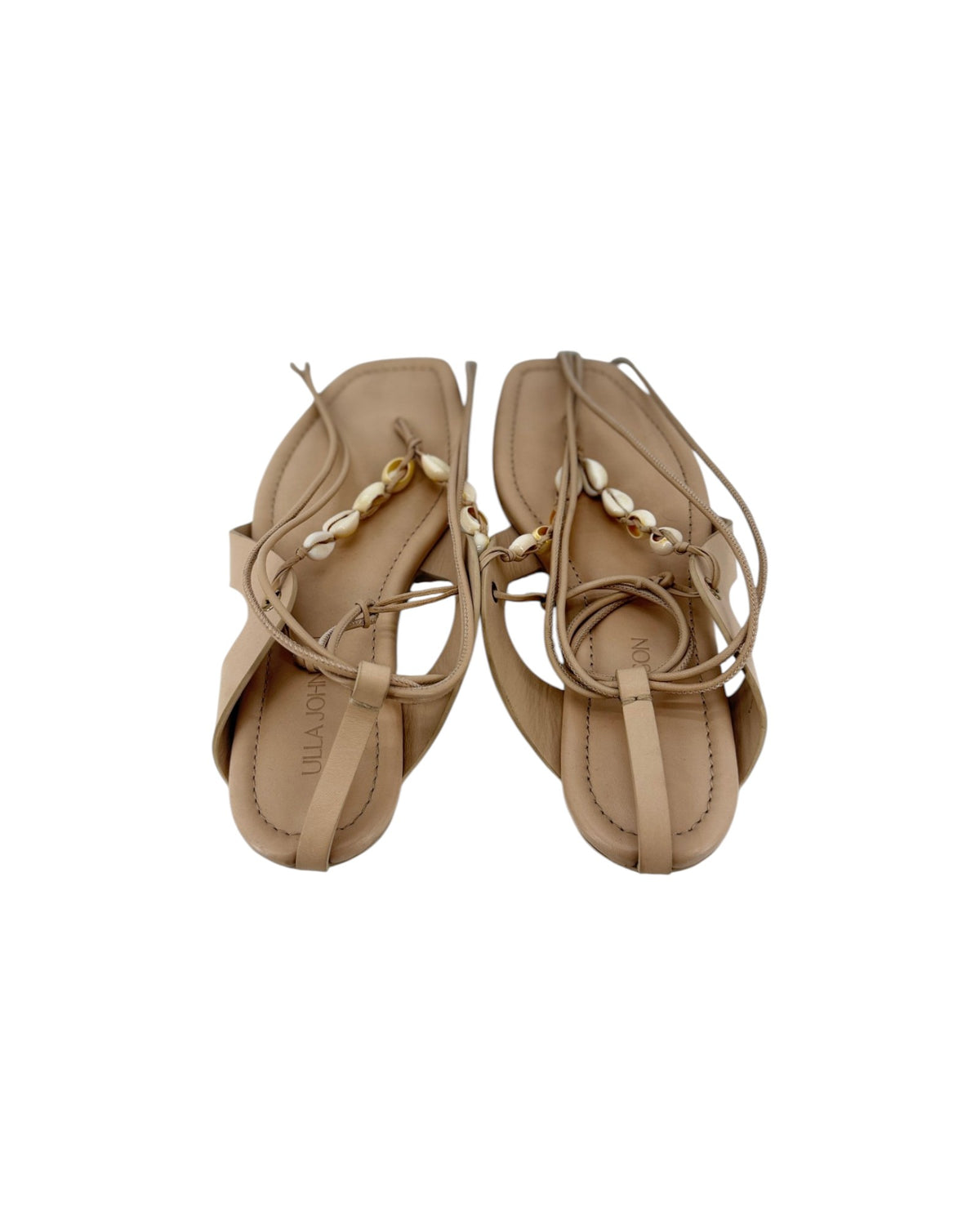 A pair of leather thong sandal with long leather ankle wrap straps and seashell details on a white background