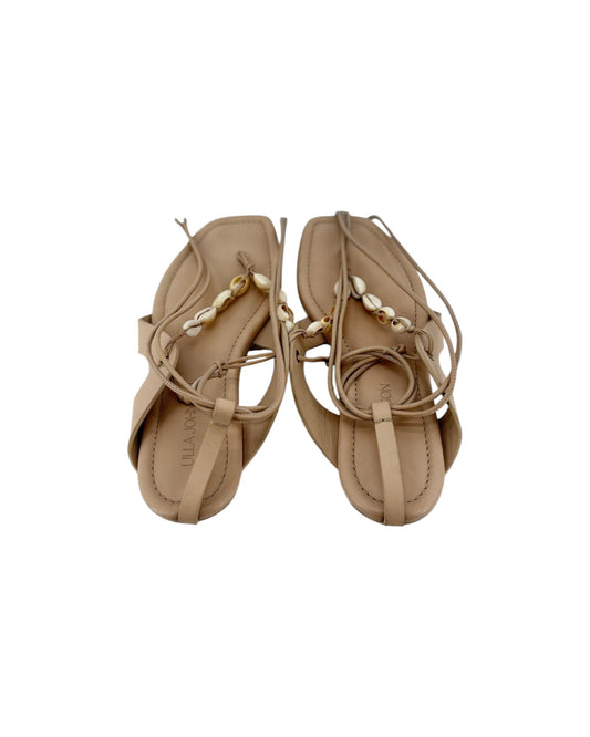 A pair of leather thong sandal with long leather ankle wrap straps and seashell details on a white background