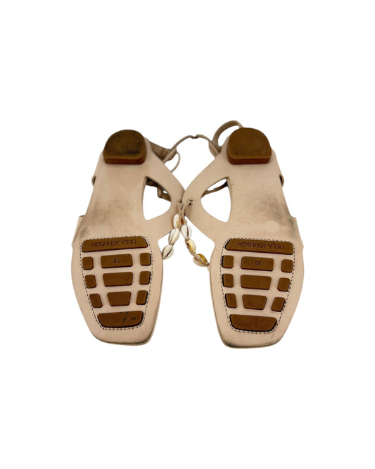 A pair of leather thong sandal soles with long leather ankle wrap straps and seashell details on a white background
