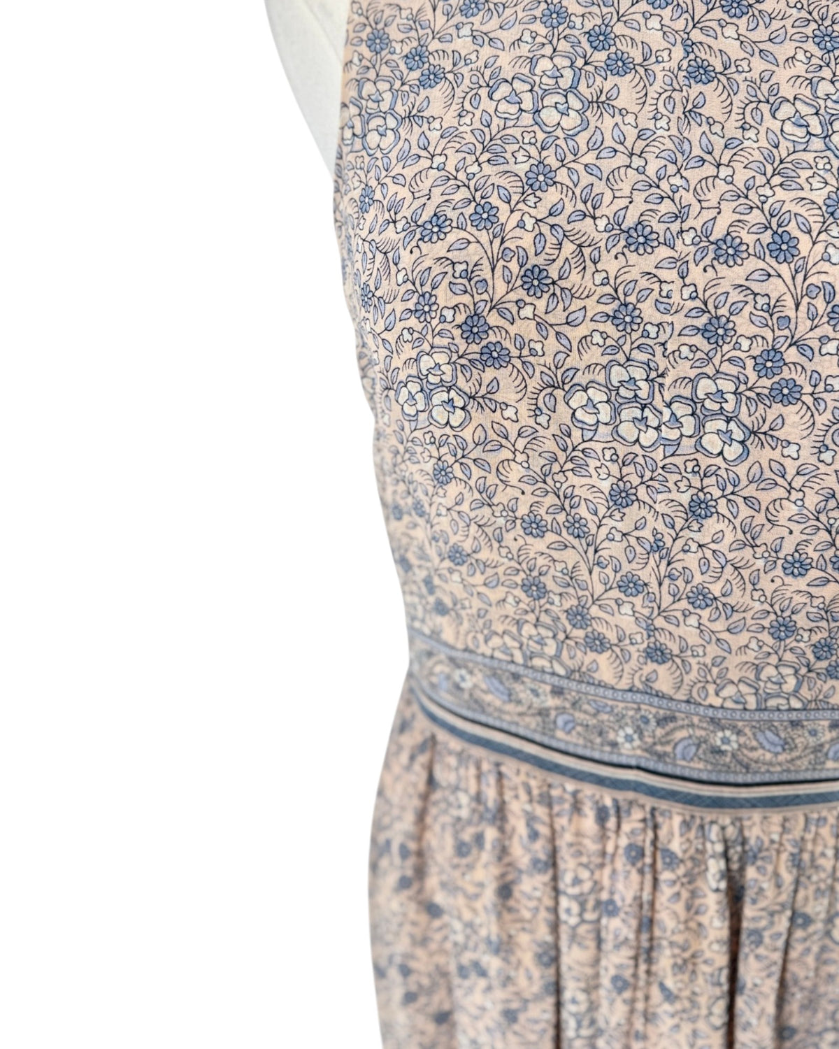 Close-up of a sleeveless dress with a beige base and blue floral block print pattern, featuring a gathered waistband.