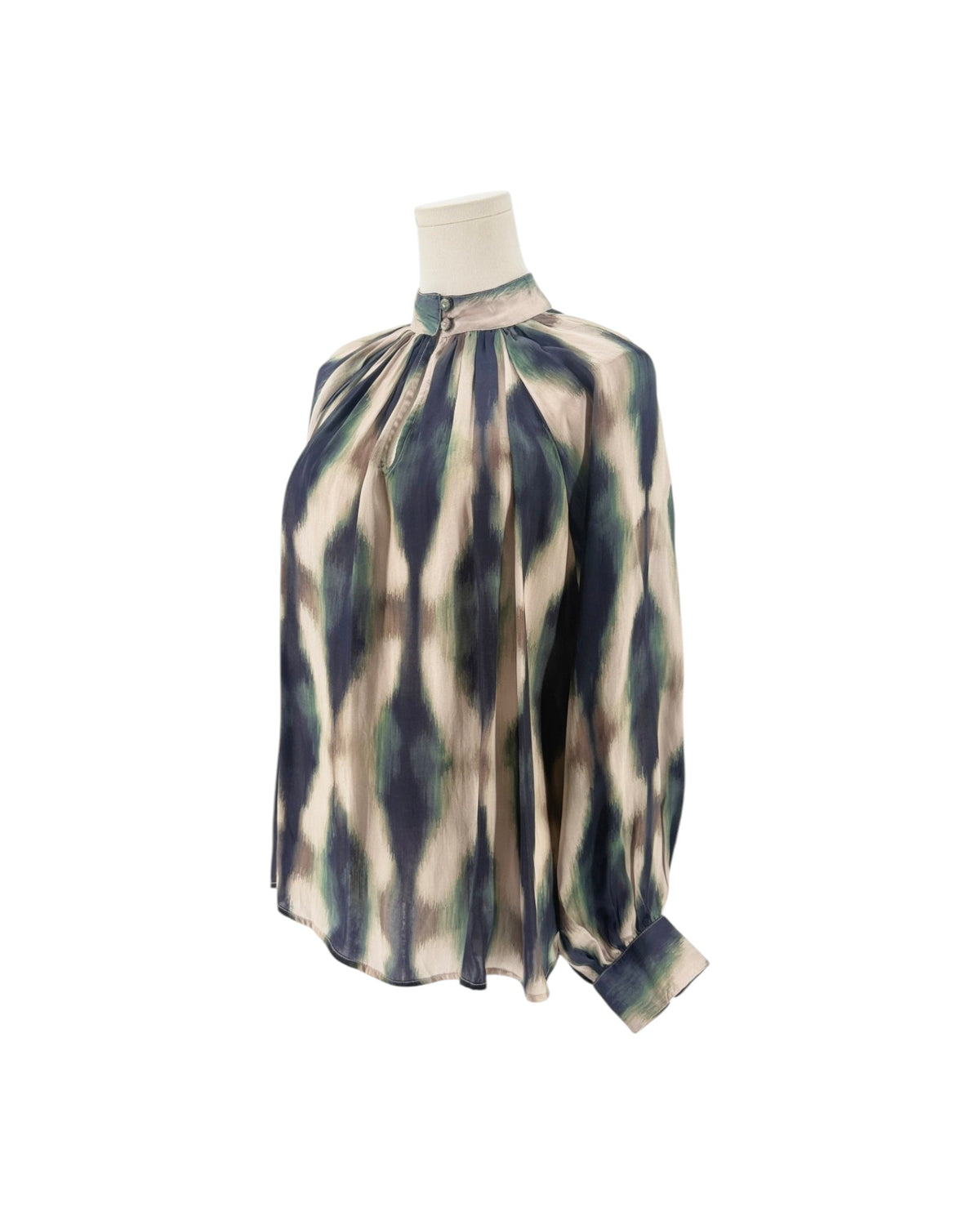 A close-up of a high-neck blouse displayed on a mannequin, featuring a pleated gathered bodice and a long sleeve. The fabric has an abstract, painterly pattern in beige, navy blue, and sage green.
