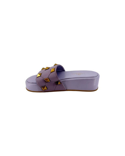 A pair of lavender slide sandals featuring a wide strap embellished with gold pyramid studs, shown from a top-down view on a white background.
