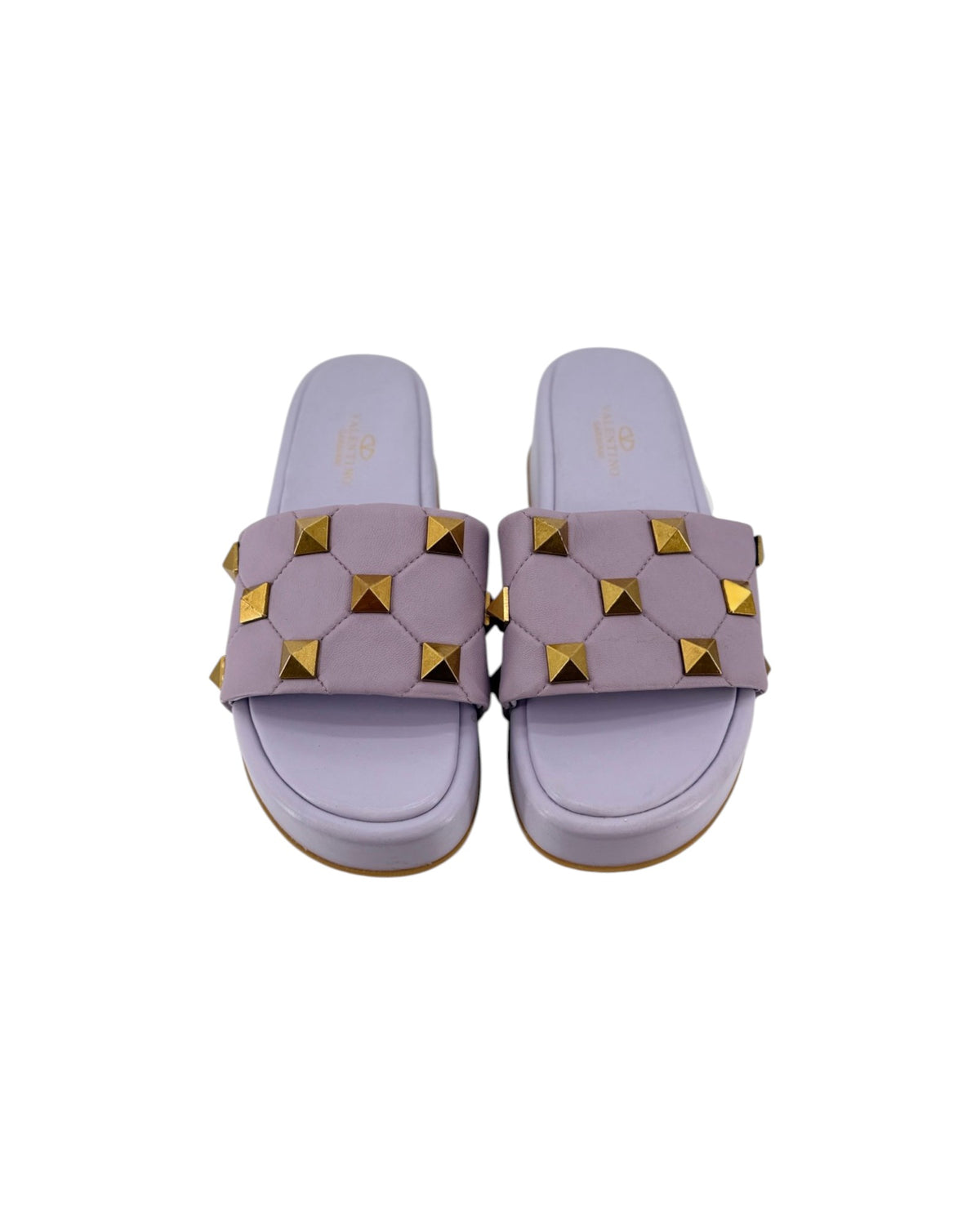 A pair of lavender slide sandals featuring a wide strap embellished with gold pyramid studs, shown from a top-down view on a white background.