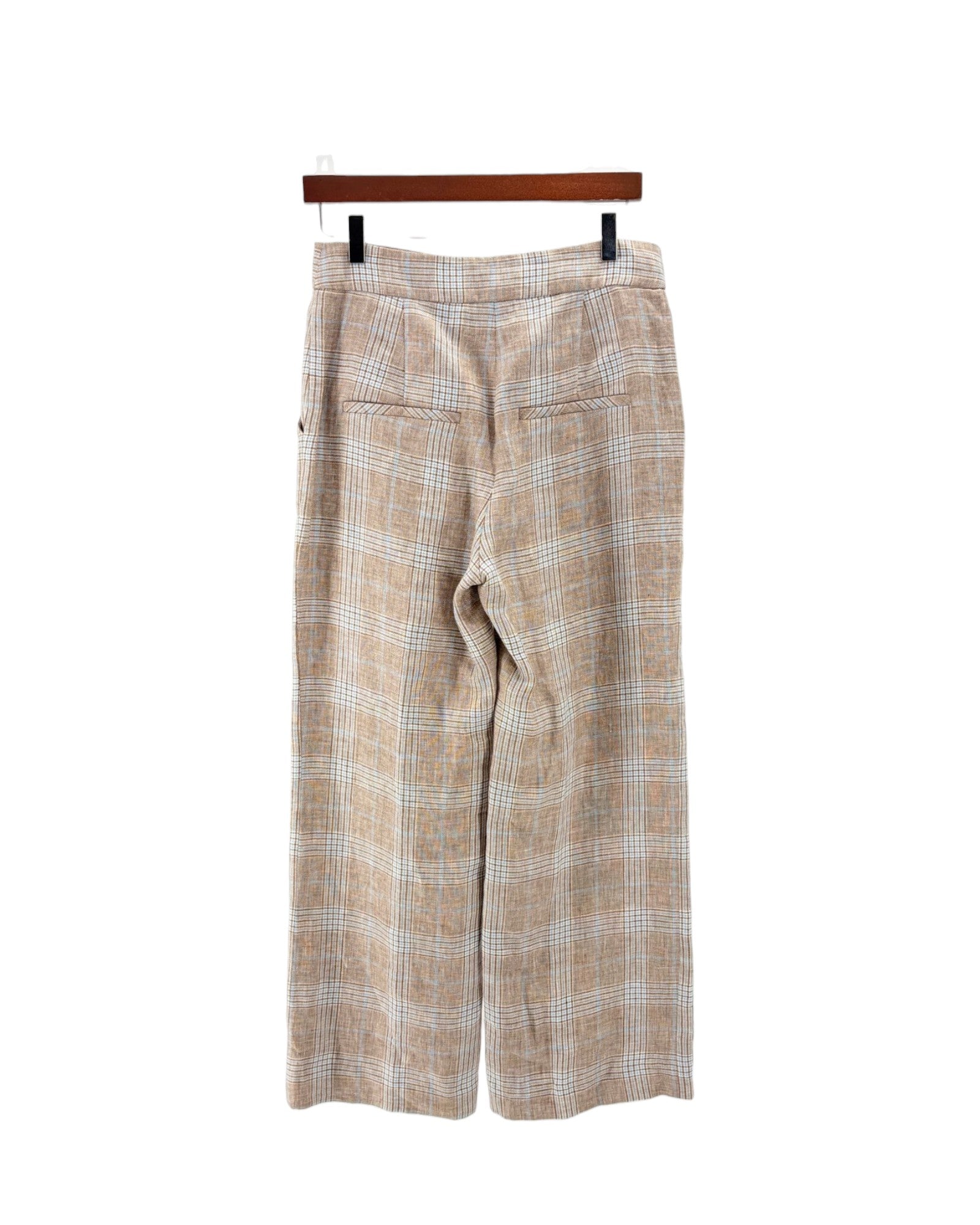A pair of wide-leg cropped trousers in a beige and white plaid pattern, hanging from a wooden hanger against a plain white background.
