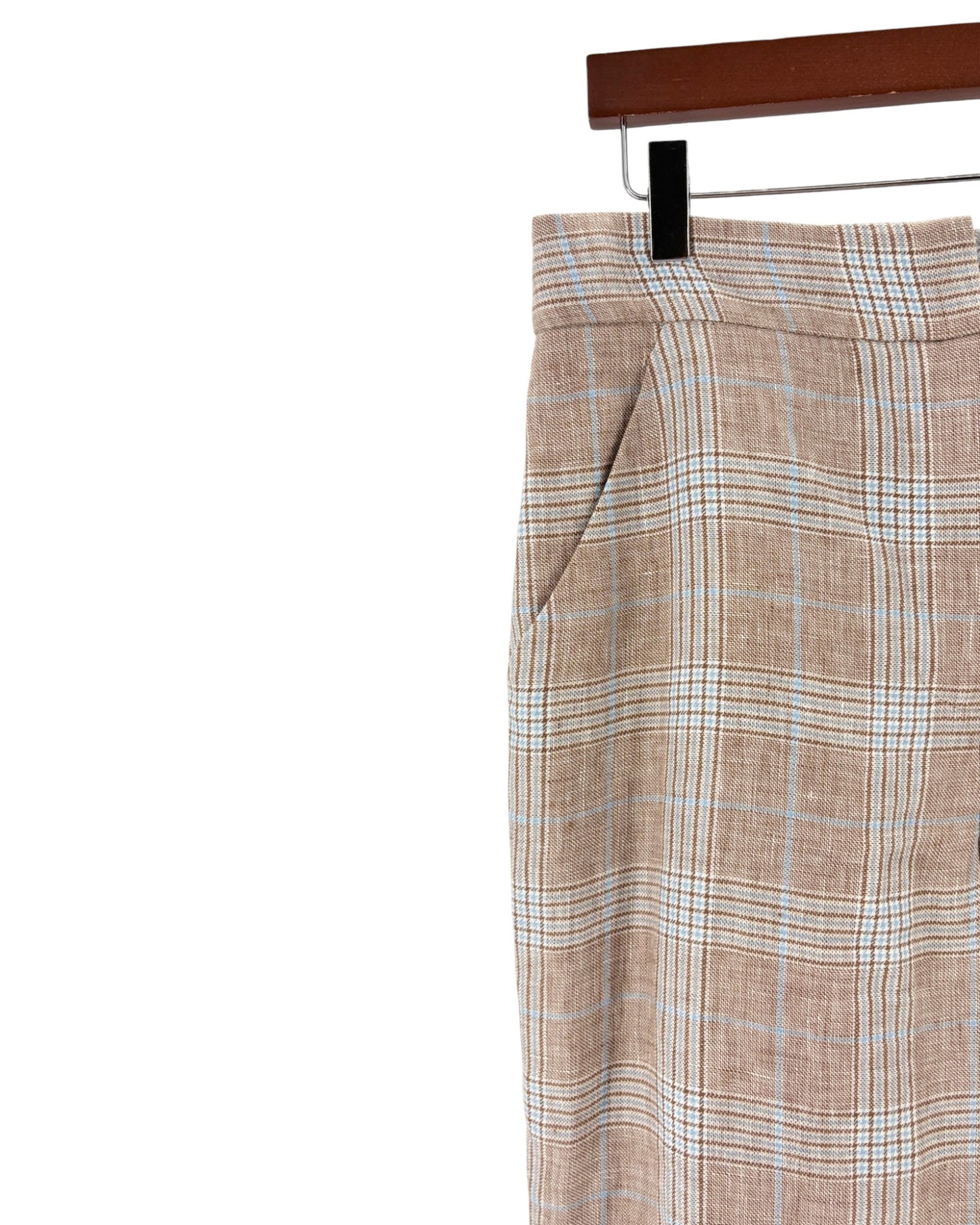 A close-up of a pair of plaid trousers hanging on a black hanger from a wooden hanger bar, set against a plain white background.