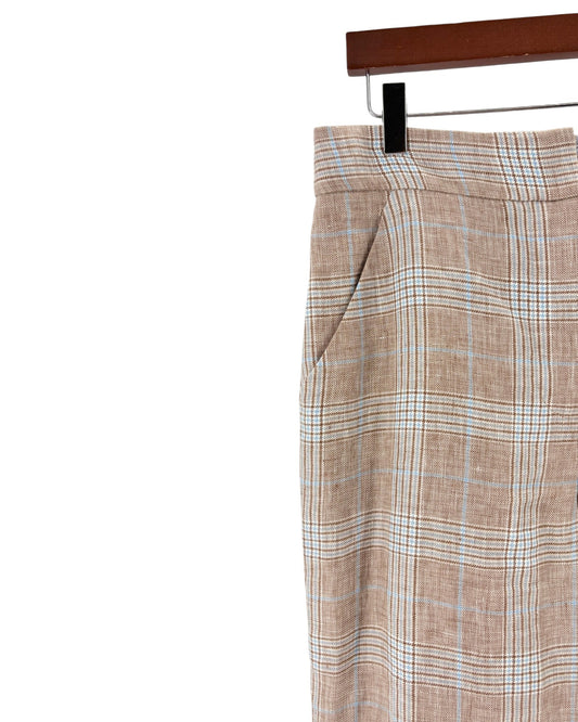 A close-up of a pair of plaid trousers hanging on a black hanger from a wooden hanger bar, set against a plain white background.