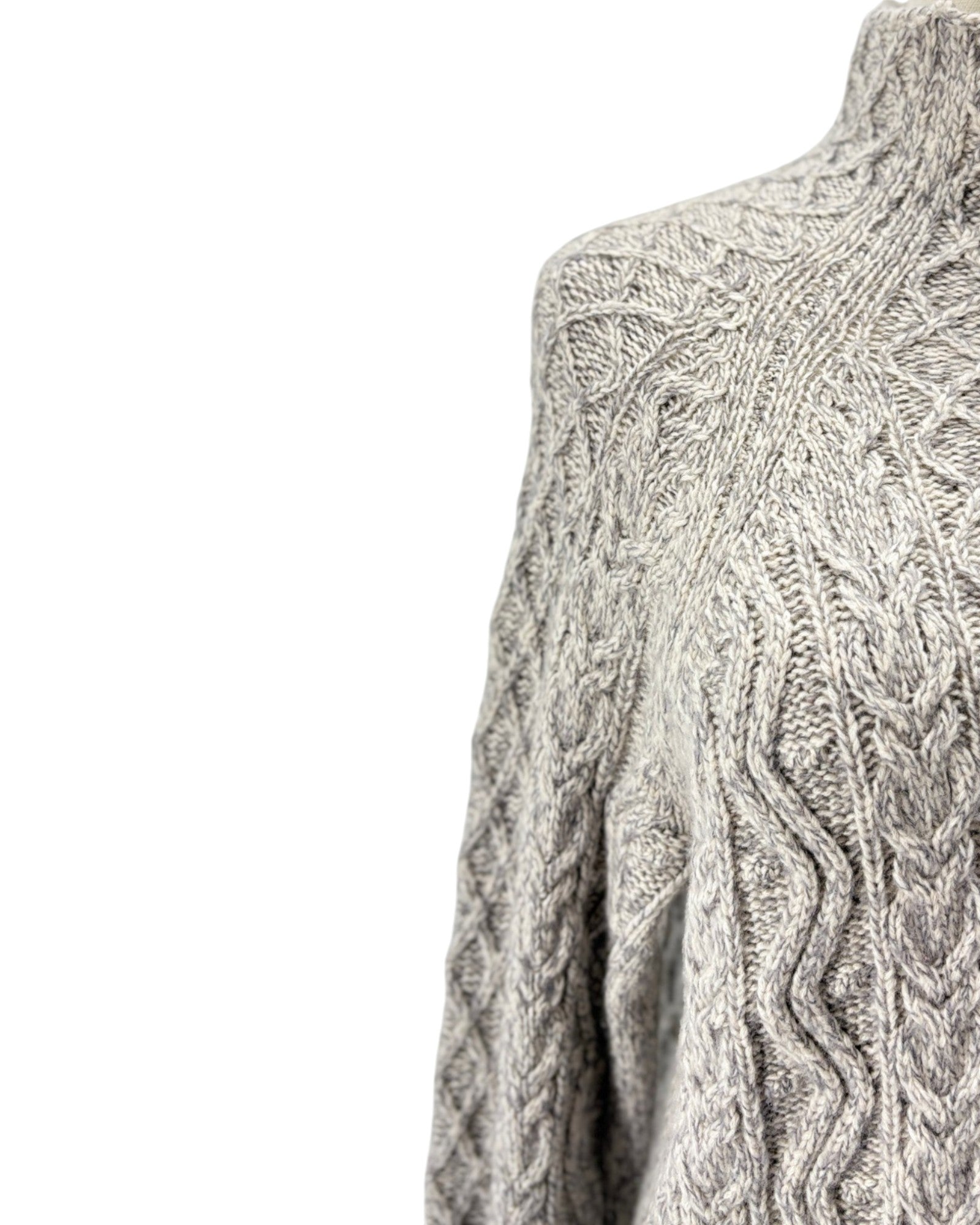 Close-up of a gray and white cable-knit sweater on a mannequin, showing the detailed knit pattern against a plain white background.