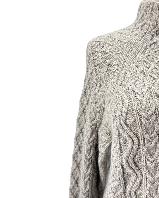 Close-up of a gray and white cable-knit sweater on a mannequin, showing the detailed knit pattern against a plain white background.