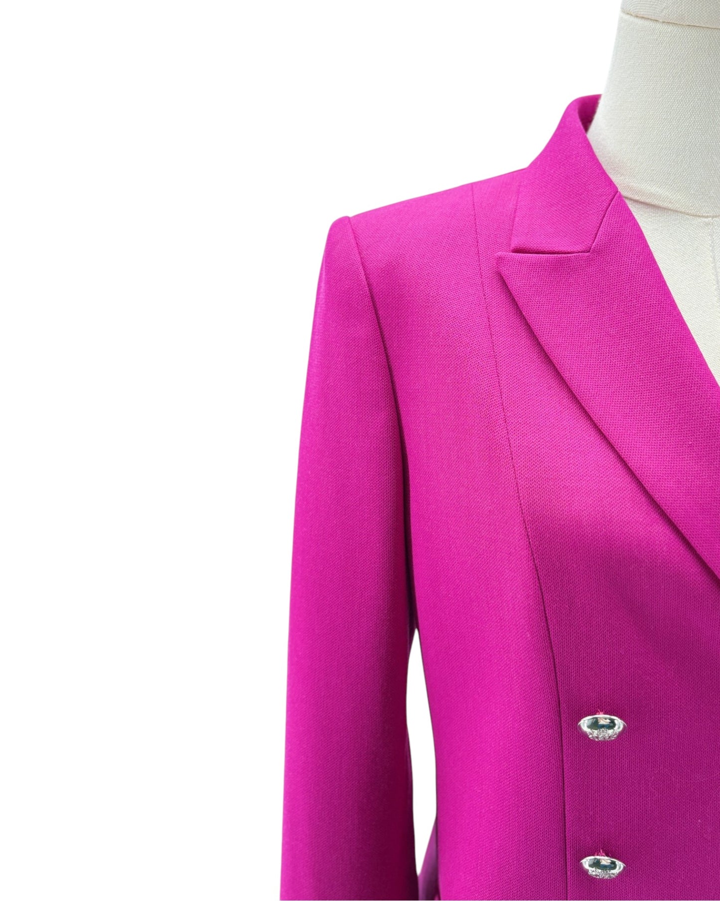 A close-up of a bright magenta pink blazer jacket displayed on a cream mannequin torso against a plain white background.