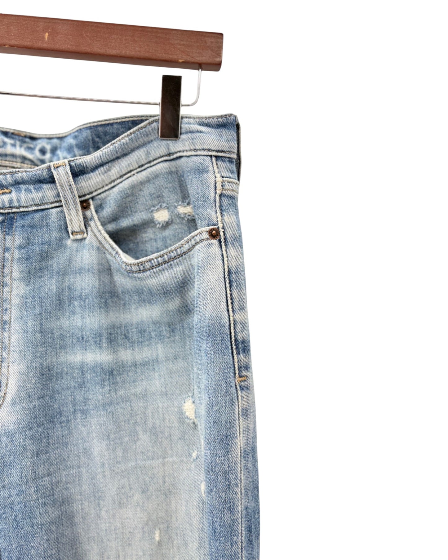 Blue denim jeans with slight distressing on a hanger against a white background