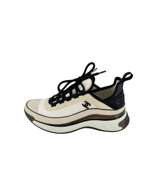 A Chanel chunky sneaker in off-white and black, featuring the iconic interlocking CC logo on the side and a thick wavy sole, shown against a plain white background.